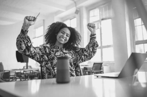 An employee smiles and raises her arms happily after learning about her pay raise.