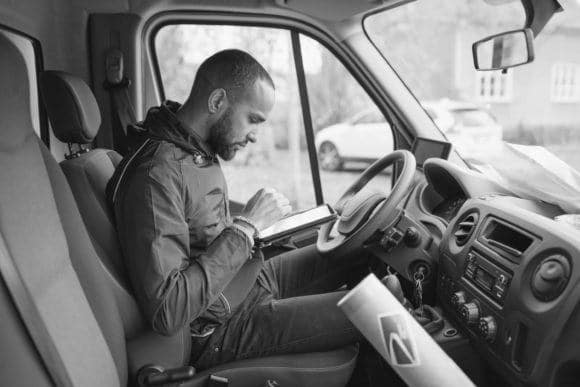 Delivery driver sitting in the front seat and entering orders into a device.
